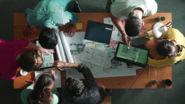 Yetenekli iş adamlarının tablet tutması ve planlara bakması. Masada dizüstü bilgisayarla dururken mimarın tasarım ve planlama bölümünün havadan görüntüsü. Sempozyum.