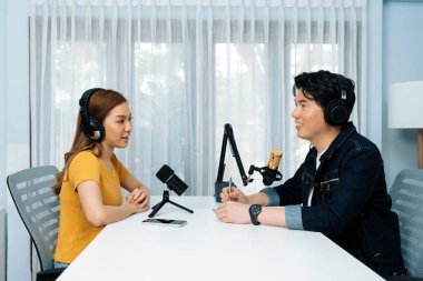 Gülümseyen radyo etkili sunucusu kulaklık takıyor kadın konuşmacı ile röportaj yapıyor sosyal medya internet sitesinden dinleyicilere bilgi paylaşıyor stüdyo kaydında sabah canlı yayın kanalı. İnfobahn.