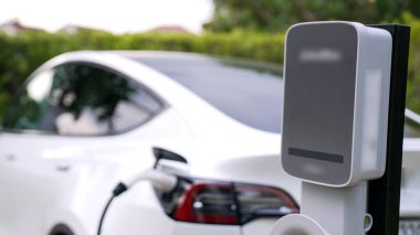 Doğal yeşil şehir parkındaki otoparkta EV elektrikli araba şarj pili. Sürdürülebilir ve çevre dostu şehir yolculuğu için yenilenebilir otomobil için alternatif temiz enerji teknolojisi. Eşzamanlama