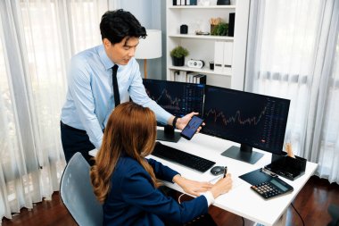 Gülümseyen işadamı cep telefonundaki dinamik borsa verilerini, iç ofisindeki internet sitesi uygulamasını analiz etmek için not yazan kadınlara gösteriyor. İnfobahn.