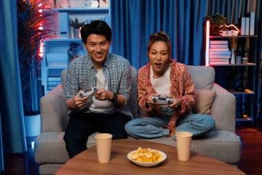 Neşeli, gülümseyen bir çiftin koltuğunda oturup oyun oynuyorlar. Oyun konsolu, hazır aperatifler ve içecekler, modern neon ışıklı, rahat oturma odasında eğlenceli bir rekabet seviyesinde. İnfobahn.