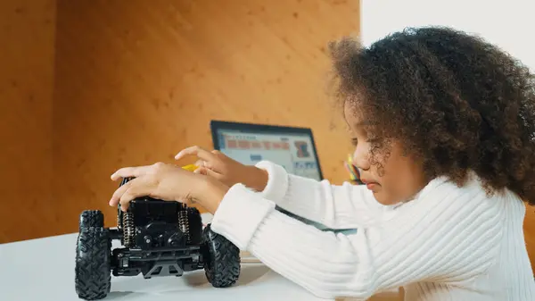 stock image Smart african girl build robotic car while using wires while using laptop setting or writing prompt code. Skilled female student working on computer in STEM technology online classroom. Erudition.