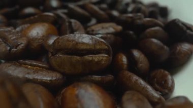 Makro kahve çekirdekleri kamerayla kaşığa saçılıyor. Beyaz kaşık kepçesiyle kahverengi kahve çekirdeklerini kapayın ve siyah arkaplanla dağılın. Kafein enerji içeceği konsepti. Pabulum.