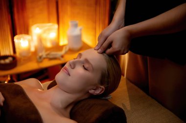 Beyaz kadın stres önleyici kafa masajı yapmaktan ve lüks otel veya otelde sıcak mum ışığında yüz güzelliği eğlencesi yapmaktan zevk alıyor. Sessiz.