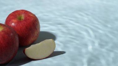 Mavi arka planda dilimlenmiş kırmızı elmaları kapatın. Elma dilimlenmiş makarnanın mavi arka planında elmacı ve suyun dökülmesi ve el sallaması. Sağlıklı beslenme ve taze üretim kavramı. Pabulum.