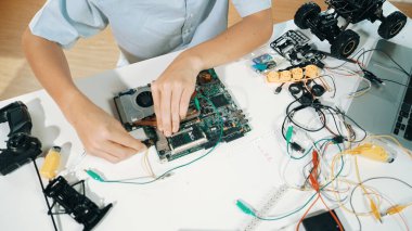 Masadaki elektronik aletle ana kartı tamir eden çocuğa yakın çekim. Elektronik teçhizatla lise öğrencilerinin elektrik panosunun en üst görüntüsü, kablo aletleri masanın etrafına saçılmış. Öğretim.