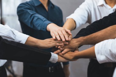 Çeşitli ofis çalışanlarından oluşan bir grup, ofis odasında el ele vererek iş sinerjisini ve iş yerindeki güçlü verimli takım çalışmasını sembolize ediyor. İş çalışanları arasındaki işbirliği ve birlik. Tedbirli