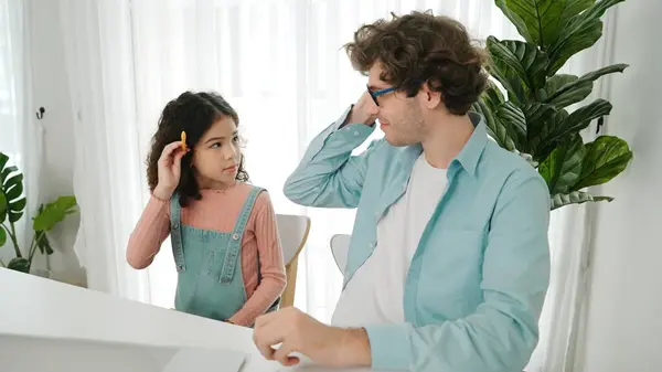 stock image Caucasian father put on pencil on ear while daughter looking at dad and put pencil on ear. Smart dad writing engineering code and generated AI by using laptop. Family spend time together. Pedagogy.