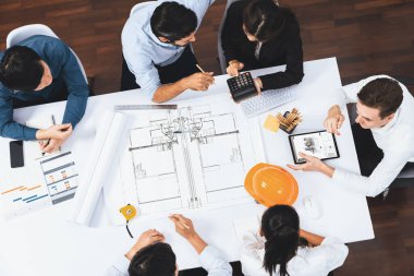 Mimari proje üzerinde birlikte çalışan, inşaat planını gözden geçiren ve toplantı masasında plan oluşturan çeşitli inşaat mühendisi ve müşteri gruplarından oluşan üst düzey bir pankart. Tedbirli