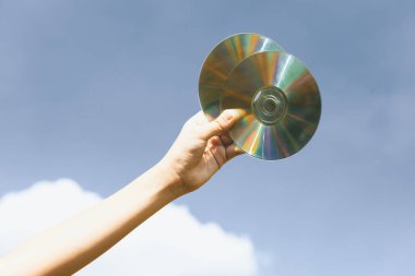 Geri dönüşümlü CD disk veya elektrik atığı gökyüzü arka planında el ele tutulur. Geri dönüşüm için elektronik çöpleri tutmak geri dönüşüm yönetimi ile temiz çevreyi geliştirmek için konsepti azaltmak ve yeniden kullanmak. Döngü