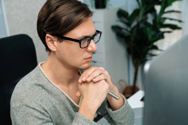 Modern ofiste oturan akıllı bir ofis çalışanı, ciddi bir yüz ifadesi olan, güzel görünümlü gözlük takan bir kamera. Yeni bir profil üzerinde sıradan bir günde çalışan iş adamı kavramı. Bireysel.