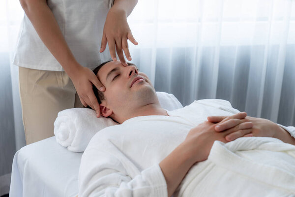 Кавказский мужчина наслаждается расслабляющим анти-стрессовым массажем головы и расслабляющим отдыхом кожи лица в дневном спа современном светлом окружении на роскошном курорте или в спа-салоне отеля. Quiescent