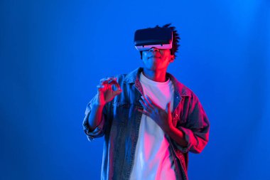 VR kullanan genç Afro-Amerikalı, boş uzay ürünlerini işaret ederek metaevren dünyasındaki mavi, neon ışıklı duvar fütüristik teknolojisi hakkında detaylı bilgi veriyor. Entrika.