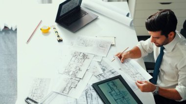 Ofiste dizüstü bilgisayar tasarımı kullanan mimar mühendisi, planlama ve ekipman dağınıklığı ile toplantı masasında otururken. Projede çalışan yetenekli inşaat mühendisi. Hizalama.
