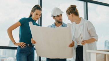 Profesyonel mimar mühendis ekibi konuşuyor, paylaşıyor, tasarım hakkında beyin fırtınası yapıyor. Yönetici planı dinlerken genç mimar plan yapıyor. İzleme