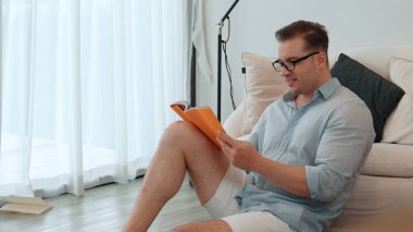 Orta yaşlı bir adam elinde kahve fincanıyla kanepede oturup ders kitabı okuyarak sosyal ve teknolojik meslekler hakkında bilgi artışı yapar ya da çocukları iyi bir yetişkin olarak yetiştirir. Hayat boyu öğrenme konsepti. Uyumsuzluk.