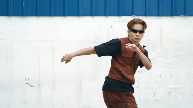 Beyaz arka planda break dans pratiği yapan yakışıklı bir sokak dansçısı. Hip hop tarzı giyinen sporcu, mavi arka planlı bir sokakta müzik eşliğinde ayak sesleri çıkarıyor. Açık hava sporu 2024 hiphop..