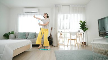 Modern apartman dairesinde dans ederken yerleri paspaslayan beyaz bir hizmetçi. Mutlu enerjik anne ya da temizlikçi müzik eşliğinde oturma odasını temizlemekten zevk alır. Yaşam tarzı. Pedagoji.