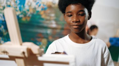 Afrikalı erkek tuvali sıcak tonda boyarken, beyaz elbiseli kız renkli duvarın arkasında havalı renkler çiziyor. Yaratıcı aktivite konsepti. Öğretim.