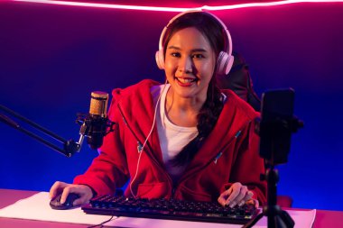 İnternet üzerinden kulaklık takıp gülümseyen Asyalı güzel kız flamasının sunucu kanalı izleyicilerle internet üzerinden konuşma yapıyor. Esport yetenekli takım oyuncuları neon mavi odada. Taktik.