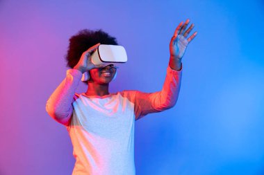 Genç Afrikalı, teknolojik dijital yenilik grafiğinde mavi neon aydınlatma grafiğinde izole edilmiş 3 boyutlu hologram veri uygulamasını seçmek için metaevren üzerinden VR gözlük takıyor. Entrika.