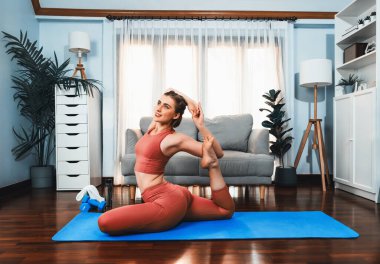 Spor kıyafetleri içinde esnek ve becerikli bir kadın evde egzersiz paspası üzerinde meditasyon pozisyonunda yoga yapıyor. Huzurlu ve huzurlu bir yoga yaşam tarzı..