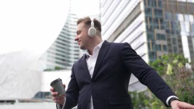 Erkek liderin etrafını sarın kulaklığı dinleyin ve neşeli ve motive edici bir şekilde rahatlatıcı müzikle dans edin. Becerikli proje yöneticisi şehir merkezinde akıllı telefon kullanırken rahat şarkılar dinlemeyi sever. Urbane.