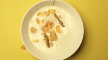 Sarı arka planı olan bir kase süte mısır gevreği bırakmanın en iyi görüntüsü. Mısır gevreğinin yavaş çekimde beyaz kaseye koyduğu kahvaltı gevreği. Sağlıklı yiyecekler. Hava görüntüsü. Sabah enerjisi, konsept. Geliştirilebilir.