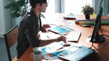 İç mimar dizüstü bilgisayarı, bilgisayarı ve kâğıdı olan toplantı masasında palete bakarken dizüstü bilgisayara bakıyor ve renk tasarlıyor. Renk tasarımı üzerinde çalışan iş adamına yakın çekim. Sempozyum.