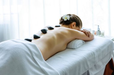 Lüks tatil köyündeki kaplıcalarda sıcak taş masajı. Gün ışığı sükunet ortamında, mutlu kadın müşteri bazalt taş masajından zevk alıyor. Rahatlatıcı bir sıcaklıkla vücudun üzerinde süzülüyor. Sessiz.