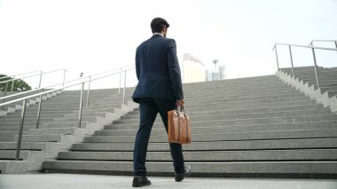 Akıllı bir iş adamının elinde çantayla merdivenlerden yukarı çıkışının en üst görüntüsü. Profesyonel proje yöneticisi merdivenlerden çıkıp işyerine gidiyor. Yeteneklerini arttırmak, terfi almak, seyahat etmek. Sevinçli..