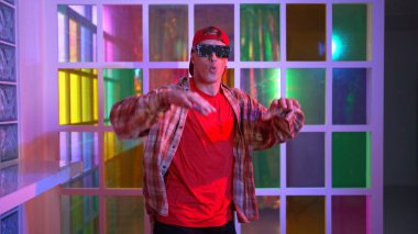 Komik break dansçı kameraya bakarken hiphop 'a doğru serbest adım atıyor. Çılgın mutlu hipster dans edip sokak dansı yaparken Led ışığında günlük kıyafet ve güneş gözlüğü takıyor. Mutluluk.