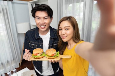 Gülümseyen sunucu şefler akıllı telefonlarıyla fotoğraf çekiyorlar. Özçekim yoluyla. Yemek programında çift hamburger tutuyorlar. İnfobahn.