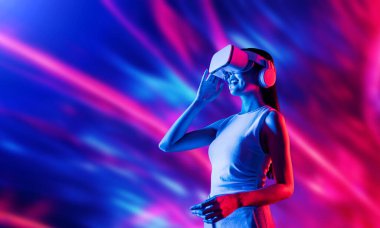 Zeki bir kadın, metaevreni birbirine bağlayan VR kulaklık takan neon ışıklarla çevrili duruyor. Gelecekteki siber uzay topluluğu teknolojisi. Uzaklara bakan zarif bir kadın ve tatmin edici bir şekilde gülümsüyor. Halüsinasyon.