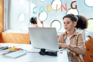 Sınıfta oturan ve diğer çocuklar dışarıyı izlerken bilgisayarla uzaktan kumanda mühendisliğini öğrenen öğrenci. Devre teli, anakart ve defter dağınık bir şekilde masaya konmuş. Etkinlik.