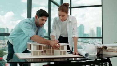 Profesyonel kooperatif iş arkadaşı ev modelini incelerken kalem kullanarak mimari modeli işaret eden yetenekli proje yöneticisi. Mimar mühendis takımı modeli belirlemek için birlikte çalışıyor. İzleme