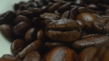 Makro kahve çekirdekleri kamerayla kaşığa saçılıyor. Beyaz kaşık kepçesiyle kahverengi kahve çekirdeklerini kapayın ve siyah arkaplanla dağılın. Kafein enerji içeceği konsepti. Pabulum.