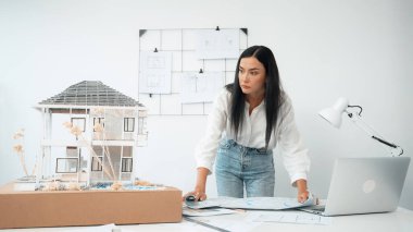 Genç, güzel beyaz bir mimar masanın üzerine plan koyar ve ev modeliyle karşılaştırırken, modern ofisteki fahişe modellerini dikkatlice incelerken arkadaki çizgilerle karşılaştırır. Tertemiz..