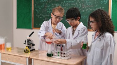 Çocuklar laboratuvarda karatahta başında dururken fen dersinde deney yapıyorlar. Mutlu öğrenci biyokimyasal sıvıyı keşfederken ve incelerken ve karıştırırken. Pedagoji.