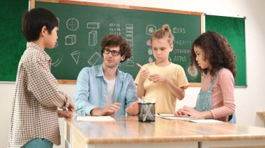 Zeki öğretmen, çeşitli çocuklar sınıf çalışması yapmak için birlikte çalışırken farklı çocukların zihin haritası çizdiği fikri açıklıyor. Çekici eğitmen öğretmek ve çalışmak hakkında konuşmak. Pedagoji.