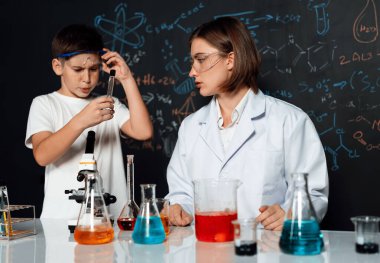 Öğretmen, laboratuarda öğrenciyi destekliyor. Öğrenci ve öğretmen cam kapta sıvı kullanarak STEM sınıfında kimya bilimi üzerine deney yapıyorlar. Karıştırma çözeltisi. Etkinlik.