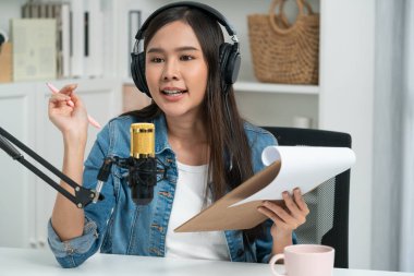 Sosyal medyada kulaklıkla canlı yayın yapan Asyalı sunucu modern stüdyoda yaşam koçluğu veya pazarlama dinleyicilerini selamlıyor. Taktik.