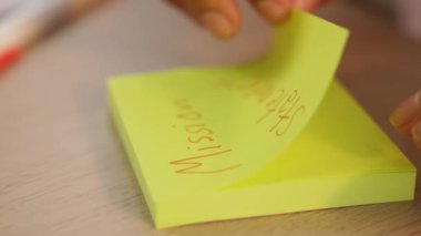 Yavaş çekimde, kadın iş kadını el yazısı pazarlama kâğıdı üzerine kalem ve yapışkan notlarla masaya yerleştirilmiş. Yaratıcı bir girişim ve takım çalışması konsepti. Eline odaklan. Değiştirilmiş.