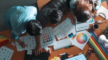 Tasarımcı fikirleri yazarken proje yöneticisinin yukarıdan aşağıya bakan görüntüsü. Akıllı iş adamları logo tasarımı fikrini açıklarken tasarımcılar palete bakarken temayı seçiyorlar. Sempozyum.