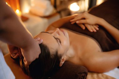 Beyaz kadın stres önleyici kafa masajı yapmaktan ve lüks otel veya otelde sıcak mum ışığında yüz güzelliği eğlencesi yapmaktan zevk alıyor. Sessiz.