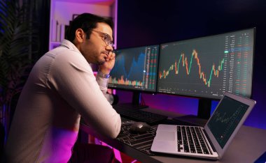 Akıllı tüccar işadamı, karanlık oda gecesinde neon ışıklı ofisteki arama pazarında yüksek kârla ekranda bilgisayar ve bilgisayar üzerinde dinamik borsa yatırımları üzerinde yoğunlaşıyor. Tahmin et..