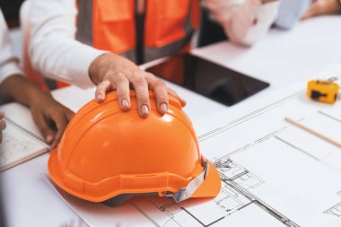 Mimari proje üzerinde birlikte çalışan çeşitli inşaat mühendisi ve müvekkil grupları, inşaat planını gözden geçirip toplantı masasında plan oluşturuyorlar. Tedbirli