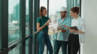 Proje yöneticisi ev modelini elinde tutarken, mimar mühendis takımı da ev tasarımı veya bina inşaatı hakkında fikir alışverişinde bulunuyor. Şehrin penceresinin yanında iç mimar duruyor. İzleme