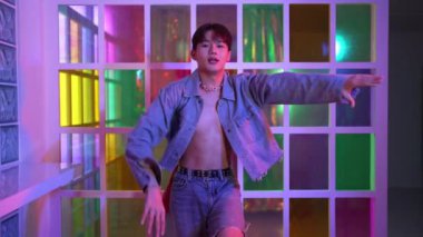 Kameraya bakarken kollarını esneten seksi kıyafetli Asyalı dansçı. Profesyonel sanatçı gece kulübünde renkli neon ışıkları canlı bir şekilde dururken serbest stil dansı yapıyor. Mutluluk.