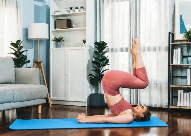 Spor kıyafetleri içinde esnek ve becerikli bir kadın evde egzersiz paspası üzerinde meditasyon pozisyonunda yoga yapıyor. Huzurlu ve huzurlu bir yoga yaşam tarzı..